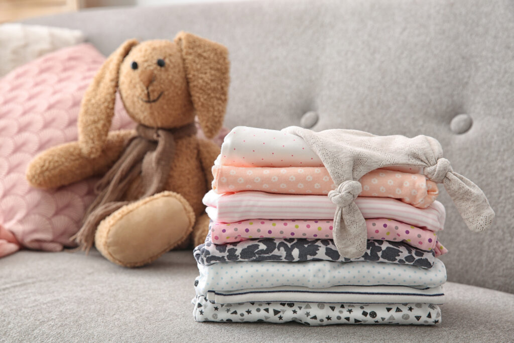 Toy bunny and stack of stylish child clothes on sofa